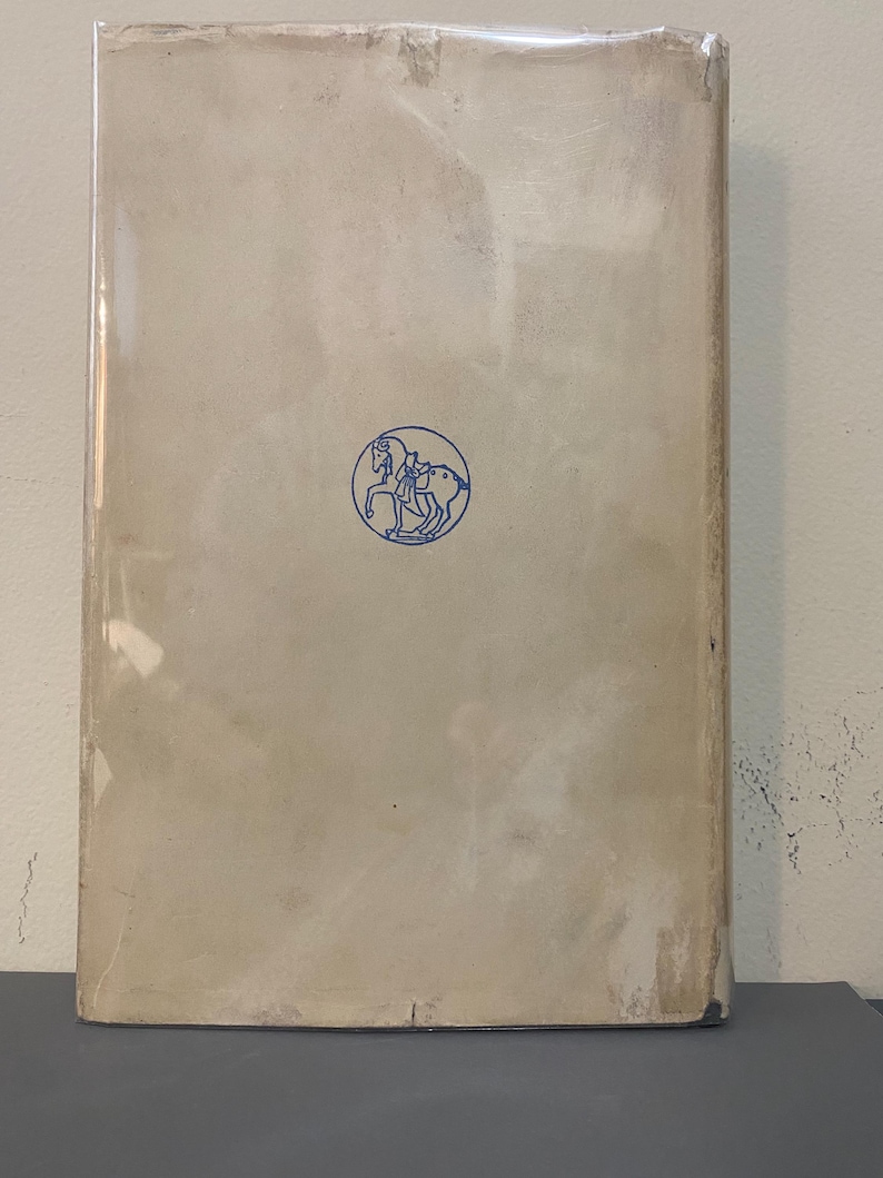 May include: A vintage book with a light beige cover, encased in clear plastic. A blue circular emblem of a person riding a horse is centered on the cover. The book's spine and edges show signs of wear.