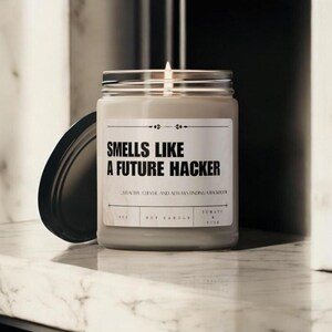 以下が含まれることがあります： 黒いラベルに「未来のハッカーの匂い。ステルス性があり、賢く、常に裏口を見つける。」と書かれた白い大豆ろうそく。