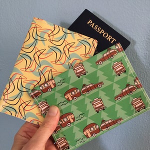 May include: Two passport covers, one with a yellow background and a boomerang pattern, and the other with a green background and a pattern of cars with trailers. The word "PASSPORT" is visible on a black passport.