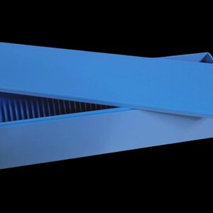 Puede incluir: Una caja rectangular azul claro con una tapa a juego, parcialmente abierta. El interior de la caja tiene crestas verticales. La caja est&aacute; sobre un fondo negro.