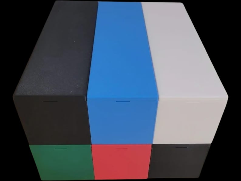 Puede incluir: Un cubo de almacenamiento multicolor con seis lados, cada uno de un color diferente: negro, azul, blanco, verde, rojo y un segundo negro. Cada lado tiene una peque&ntilde;a ranura horizontal. El cubo est&aacute; sobre un fondo negro.