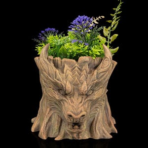 May include: A brown dragon-shaped planter, filled with artificial purple and green plants. The planter has a textured, wood-like appearance with carved details, including horns and a fierce expression. The background is black.