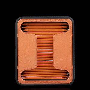 May include: A rectangular storage organiser with a black outer frame and a textured copper-coloured interior structure. The unit holds a stack of orange rectangular packets with thin red stripes, arranged horizontally within the central opening.