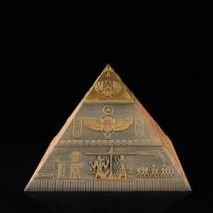 May include: A detailed, gold and gray pyramid with intricate Egyptian hieroglyphs and carvings. The pyramid features a golden scarab beetle and other ancient symbols, showcasing a historical theme. The pyramid is set against a black background.