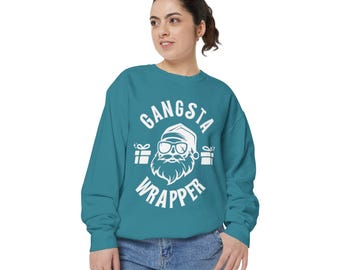 Pode incluir: Camisola azul turquesa com um gráfico branco de um Papai Noel de óculos de sol e segurando presentes. O texto "Gangsta Wrapper" é impresso em torno do gráfico do Papai Noel.