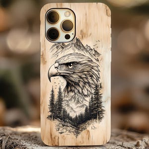 Könnte beinhalten: Eine Handyhülle aus Holz mit einer Schwarzweißillustration eines Adlerkopfes und einer Bergszene. Die Hülle hat eine natürliche Holzmaserung.
