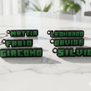 May include: Black and green keychains with names in a pixelated font. The names include Mattia, Fabio, Giacomo, Leonardo, Davide, and Silviu. Each keychain has a silver keyring attached.