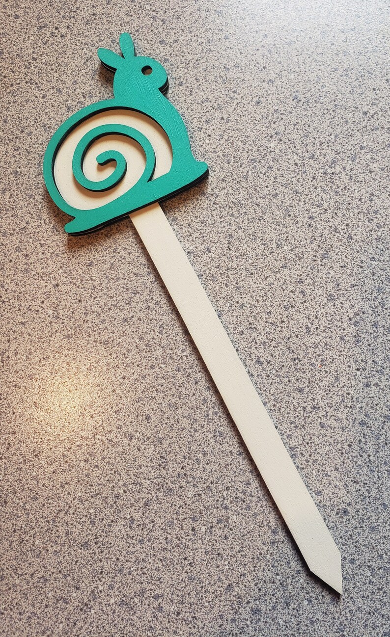 May include: A teal wooden snail garden stake with a white stick. The snail has a spiral shell.