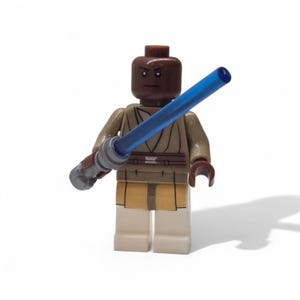 May include: A Lego minifigure of a Star Wars character. The figure has a dark brown head, tan robes, and a blue lightsaber. The figure is standing on a white surface.