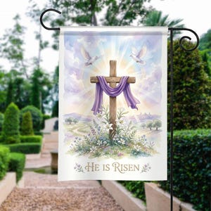 May include: A garden flag featuring a watercolor illustration of a wooden cross draped with a purple cloth, with two white doves and the text "He Is Risen." The background shows a sunny sky, rolling hills, and flowers.