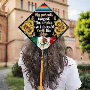 May include: A graduation cap with a black diamond design featuring sunflowers, butterflies, and the text "My parents crossed the border so I could cross the stage." The cap includes the Mexican flag and a gold tassel.