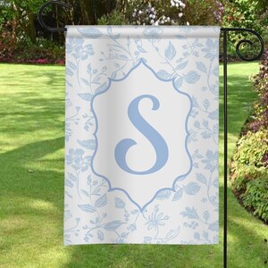 May include: A white garden flag with a blue floral pattern and a blue letter "S" in a white frame.
