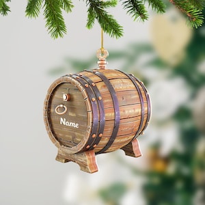 May include: A wooden barrel-shaped Christmas ornament with a metal ring and the word "Name" inscribed on the side. The ornament is brown and has a rustic look.