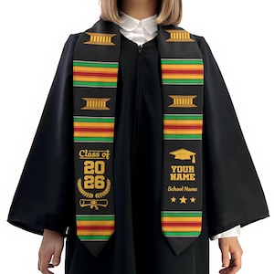 May include: Black graduation sash with gold text and colorful stripes. The sash displays "Class of 2026" and a diploma graphic. The other side has a graduation cap and space for a name and school.