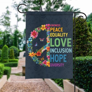May include: A garden flag with a peace sign made of colorful flowers and butterflies. The words "Kindness, Peace, Equality, Love, Inclusion, Hope, Diversity" are written around the peace sign.