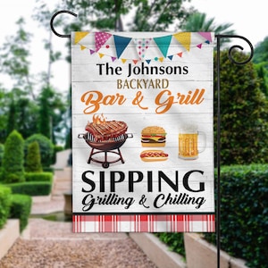 May include: A white wooden sign with the text "The Johnsons Backyard Bar & Grill Sipping Grilling & Chilling" with a red and white checkered border. The sign features a grill with a steak, a hamburger, a hot dog, and a glass of beer.