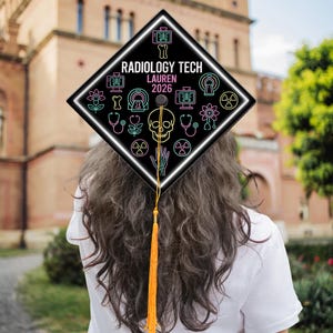 May include: A black graduation cap with a white border and neon-colored medical-themed icons. The cap reads "RADIOLOGY TECH LAUREN 2026" in white text. A gold tassel hangs from the cap.
