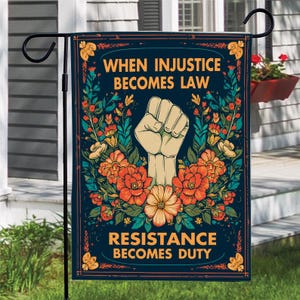May include: A garden flag with the text "WHEN INJUSTICE BECOMES LAW RESISTANCE BECOMES DUTY" and a raised fist graphic. The flag features a dark blue background with floral and leaf accents in orange, yellow, and green.