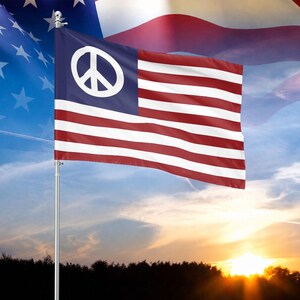 May include: A flag featuring a blue canton with a large white peace symbol, followed by horizontal red and white stripes. The flag is mounted on a silver pole against a background of a sunset sky and a partially visible American flag overlay.