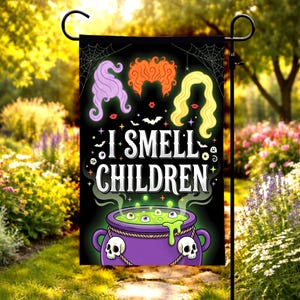May include: A black garden flag featuring three stylized hair silhouettes in purple, orange, and yellow above the white text I SMELL CHILDREN. Below the text is a purple cauldron with green bubbling liquid, eyeballs, and two white skull accents.
