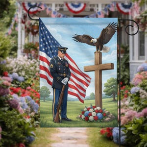 May include: A decorative garden flag featuring a soldier in a dark blue uniform standing with a rifle beside a wooden cross. A bald eagle is perched atop the cross, and a large American flag waves in the background over a grassy field.