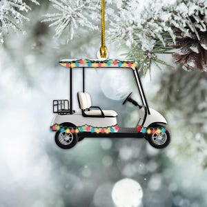 May include: White golf cart ornament with colorful Christmas lights strung around it. The cart has a white seat and steering wheel. The ornament is hanging from a gold string.