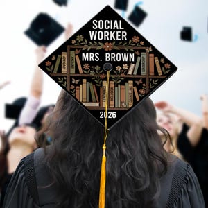 May include: A graduation cap with the words "SOCIAL WORKER MRS. BROWN 2026" in white. The cap features a bookshelf design with floral and butterfly accents. The tassel is yellow.