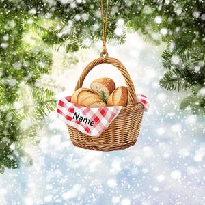May include: A brown wicker basket with a red and white checkered cloth, filled with bread rolls. The basket has a gold string attached to the top and the cloth has the word "Name" printed on it.