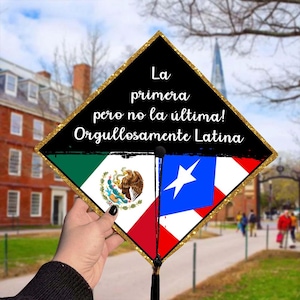 May include: A graduation cap with a black top and gold glitter trim. The cap features the flags of Mexico and Puerto Rico. Text on the cap reads "La primera pero no la última! Orgullosamente Latina."