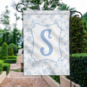 May include: A white garden flag with a blue floral pattern and a blue letter "S" in a white frame.
