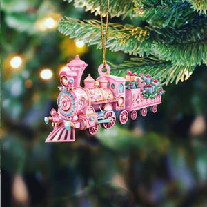 May include: Pink and gold Christmas train ornament with a name tag that says "Name". The train has a bell, wheels, and a caboose with presents and greenery.