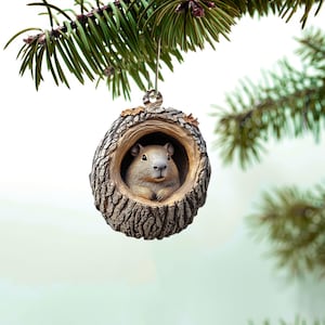 May include: A brown and gray squirrel ornament in the shape of a tree trunk with a hole in the center. The squirrel is peeking out of the hole.
