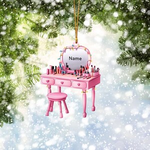 May include: Pink vanity set Christmas ornament with a mirror, drawers, and a stool. The mirror has a space for a name, "Name".