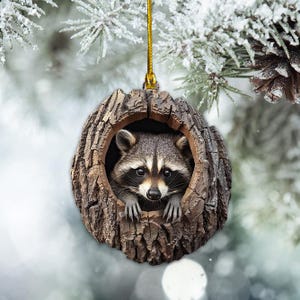 May include: A raccoon ornament with a brown and gray fur pattern peeking out of a hollowed-out tree trunk. The ornament is made of wood and has a rustic look.