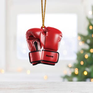 May include: Red boxing gloves ornament with a gold string for hanging. The gloves are personalized with the word "Name".