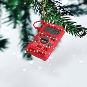 May include: A red digital multimeter Christmas ornament with a string of colorful lights wrapped around it. The display reads "13.0".