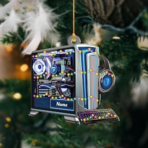 May include: A computer-themed Christmas ornament. The ornament is shaped like a desktop computer with a keyboard and headphones. The computer case is silver and black, with blue and white lights. The keyboard and headphones have colorful lights. The ornament has the word "Name" on it.