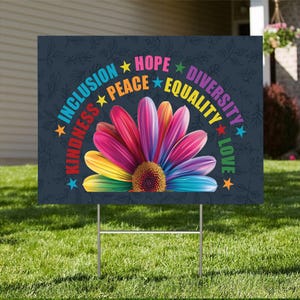 May include: A yard sign with a rainbow flower and the words "Inclusion, Kindness, Peace, Hope, Equality, Diversity, Love" around it.