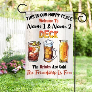 May include: A white wooden sign with the text "This is our happy place. Welcome to [Name 1] & [Name 2] Deck. The drinks are cold. The friendship is free."  The sign features illustrations of a glass of iced tea, a beer mug, and a bottle of beer.