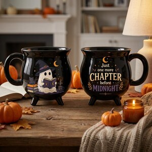 May include: Two black ceramic cauldron-shaped mugs with three small feet. One mug features a ghost wearing a witch hat reading a book, while the other displays the text 'Just one more CHAPTER before MIDNIGHT' in gold and purple lettering.
