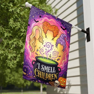 May include: A rectangular garden flag featuring a black cauldron with green liquid and the text I SMELL CHILDREN. Above the cauldron are three stylized hair silhouettes in blonde, orange, and purple, surrounded by bats, spiders, and a pumpkin.