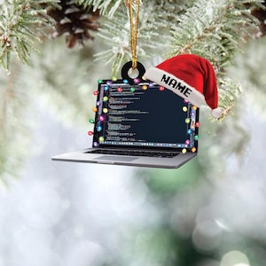 May include: A laptop Christmas ornament with a red Santa hat that says "NAME". The laptop screen displays code and is decorated with colorful Christmas lights. The ornament is hanging from a gold string.