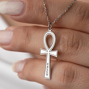 May include: A silver chain necklace with an ankh pendant. The ankh is engraved with the word "SALLY".