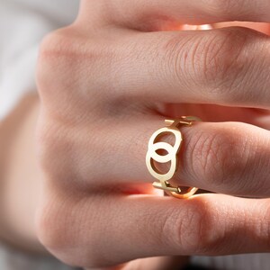 May include: A gold ring with a double circle design. The ring is worn on a finger.