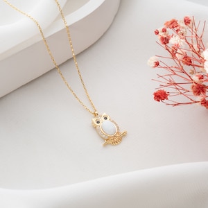 Könnte beinhalten: Eine goldene Kettenkette mit einem Eulenanhänger. Die Eule ist aus weißem Opal gefertigt und hat klare Kristall-Akzente.