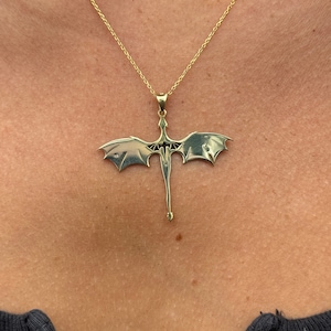 Pu&ograve; includere: Una collana con catena d'oro con un ciondolo a forma di drago. Il drago &egrave; rivolto in avanti con le ali spiegate.