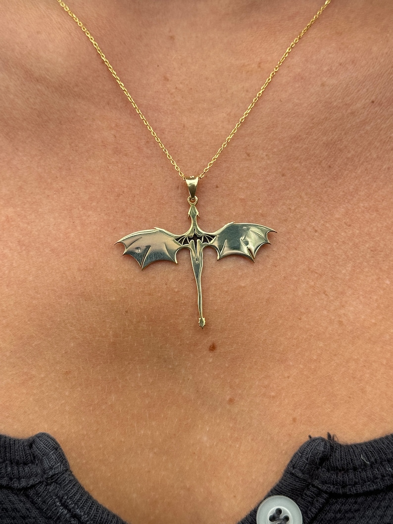 Pu&ograve; includere: Una collana con catena d'oro con un ciondolo a forma di drago. Il drago &egrave; rivolto in avanti con le ali spiegate.