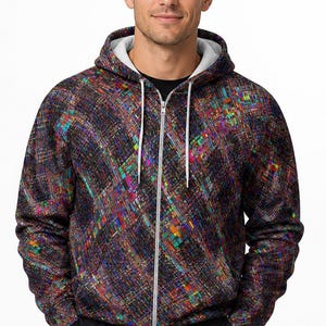 May include: A long-sleeve zip-up hoodie featuring a dark, multi-colored abstract pattern with vibrant flecks of blue, red, and yellow. The garment includes a white drawstring, a white inner hood lining, and a silver-toned front zipper closure.