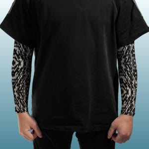 May include: A black short-sleeved t-shirt layered over long sleeves featuring a repeating geometric pattern in shades of black, white, and gray. The garment has a solid black torso and solid black short sleeves, with the patterned sleeves extending underneath.