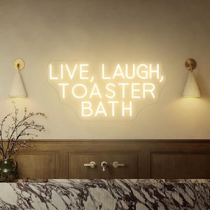 Puede incluir: Un letrero de ne&oacute;n blanco con el texto "LIVE, LAUGH, TOASTER BATH" en una pared blanca en un ambiente de ba&ntilde;o. El letrero est&aacute; iluminado y tiene un borde ondulado.